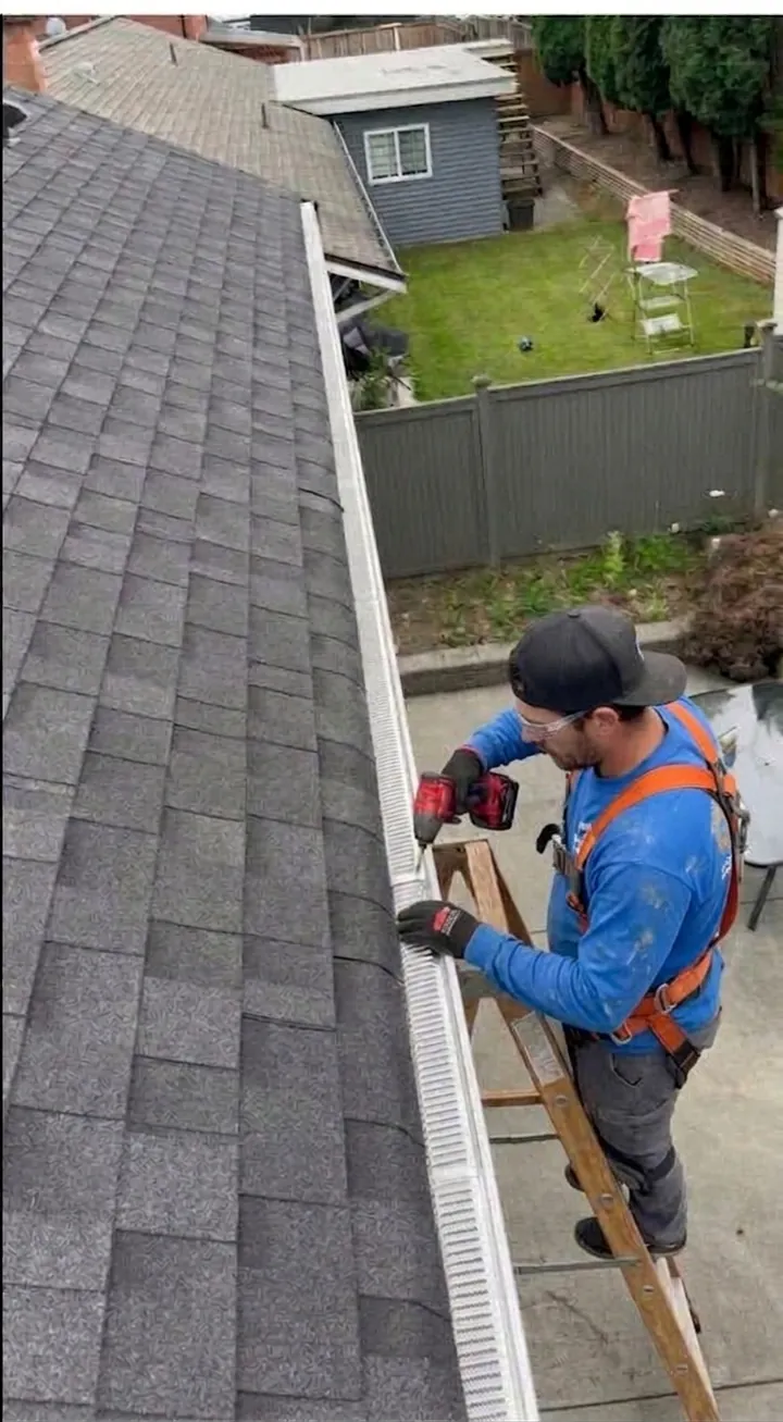 Gutter guard installation: technician on a ladder screwing a small-hole gutter guard onto the gutter