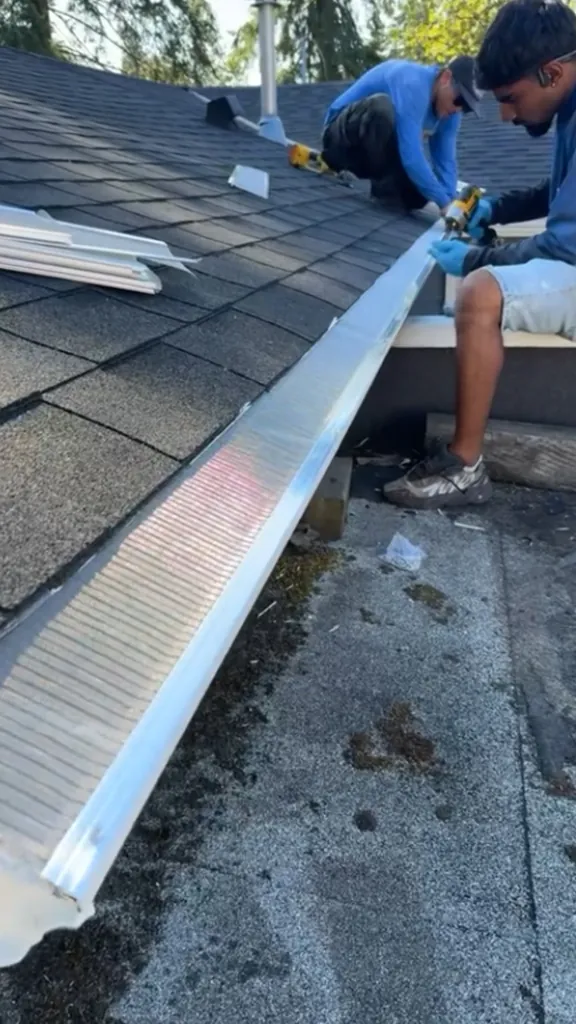 Two technicians fastening gutter guards onto a gutter with impact drivers