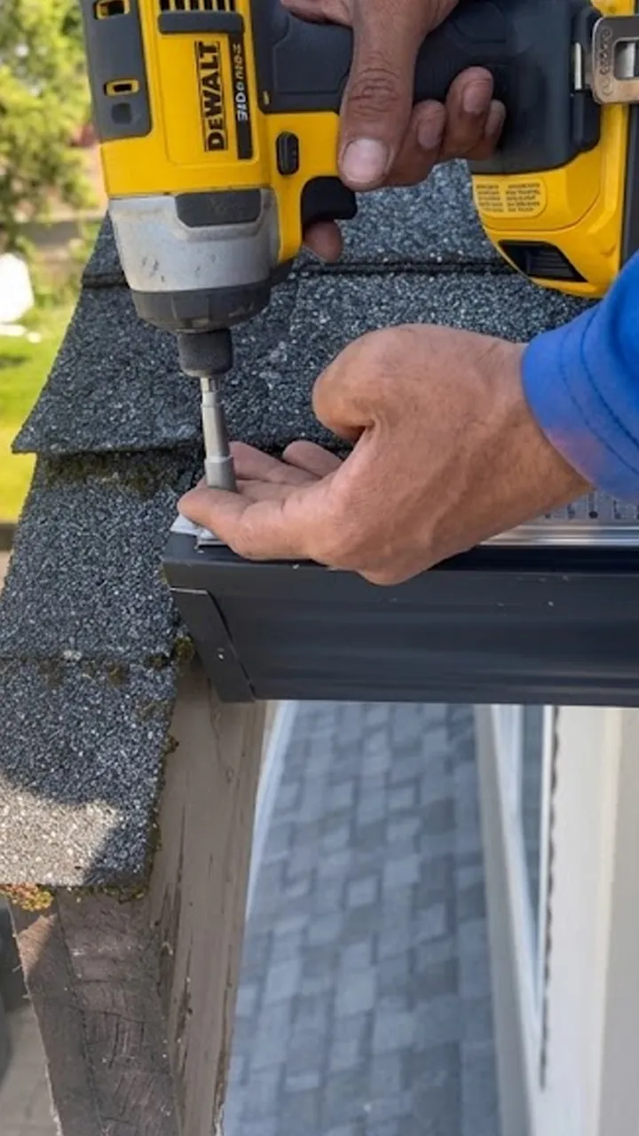 Close-up of a gutter guard being screwed onto the front of a gutter with an impact driver