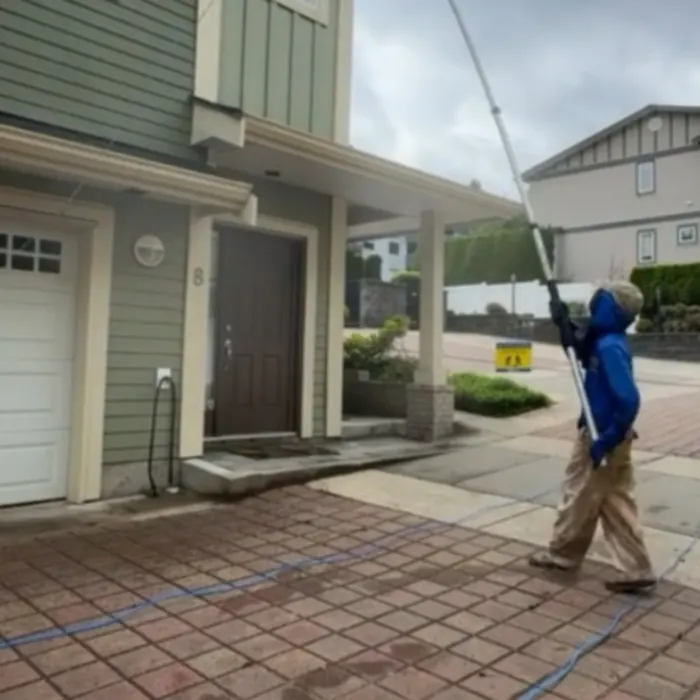 Technician reaching a third-storey townhouse wall with a water-fed pole, Surrey BC