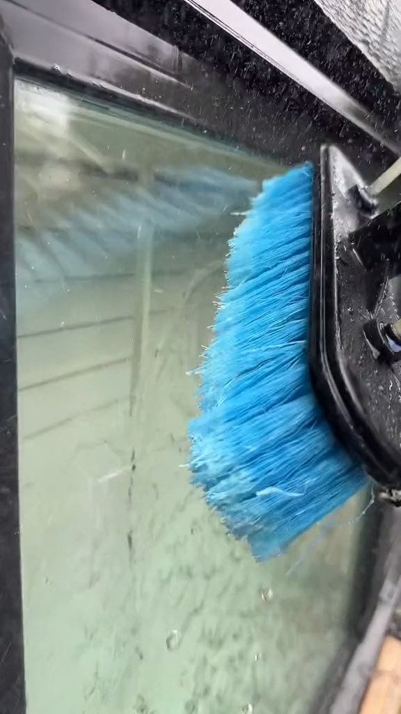 Water-fed pole brush scrubbing dirt from the outside of a window pane